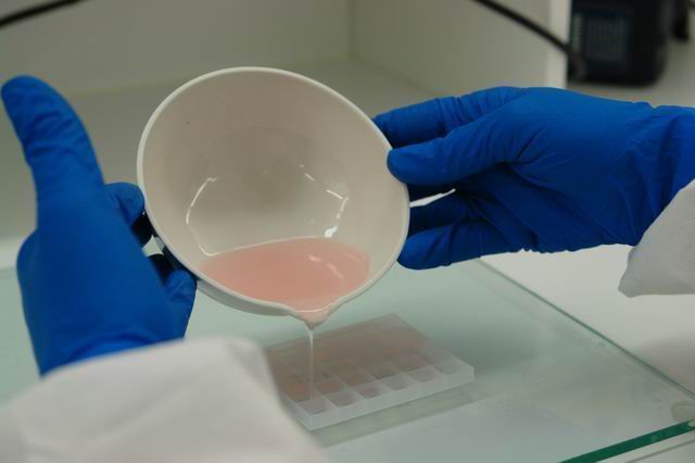 A person wearing blue gloves pouring liquid into a bowl