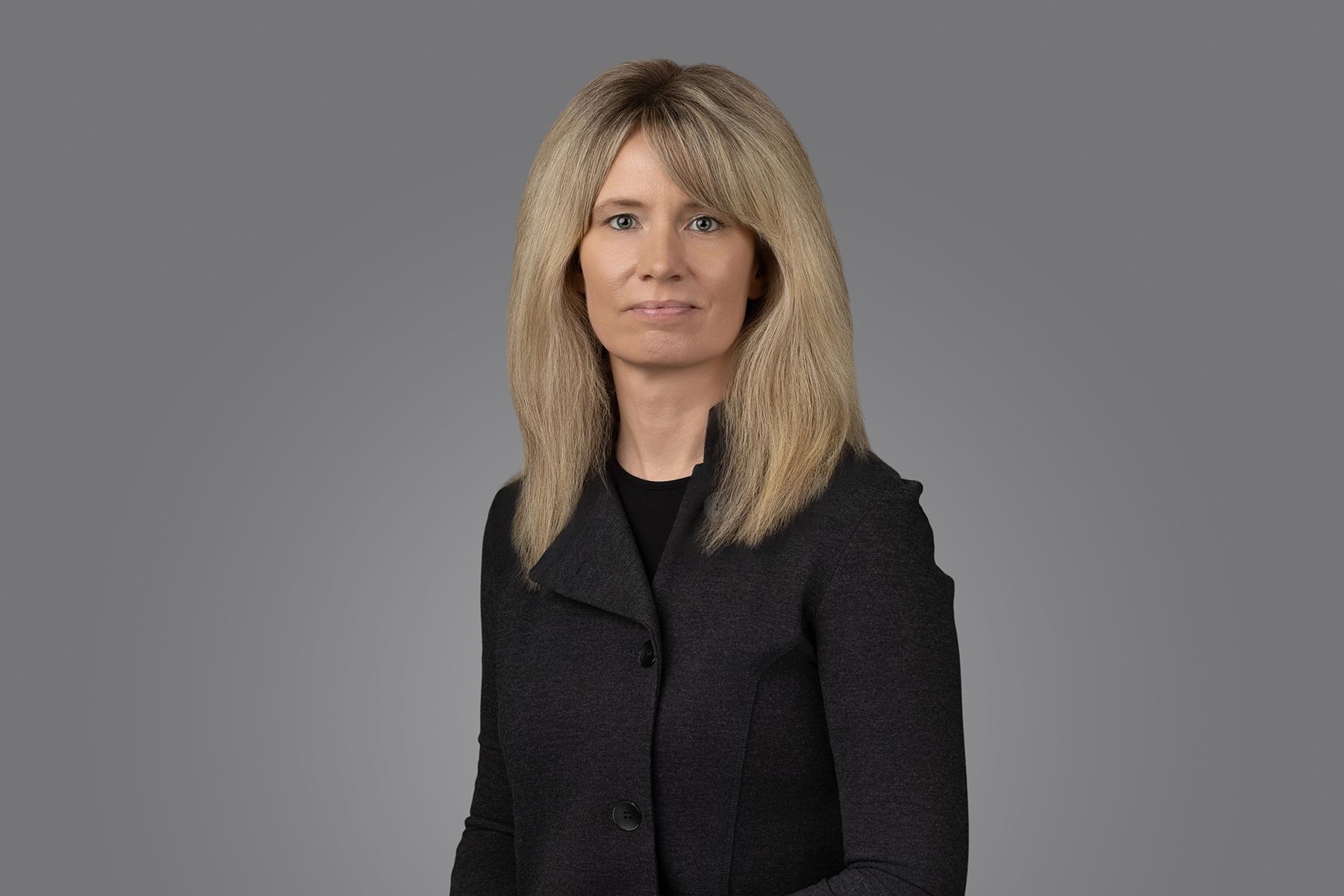 A woman in a black shirt is smiling and standing in front of a white background.