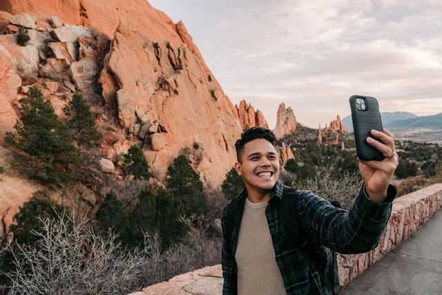 A man is taking a selfie with his cell phone in front of a mountain.