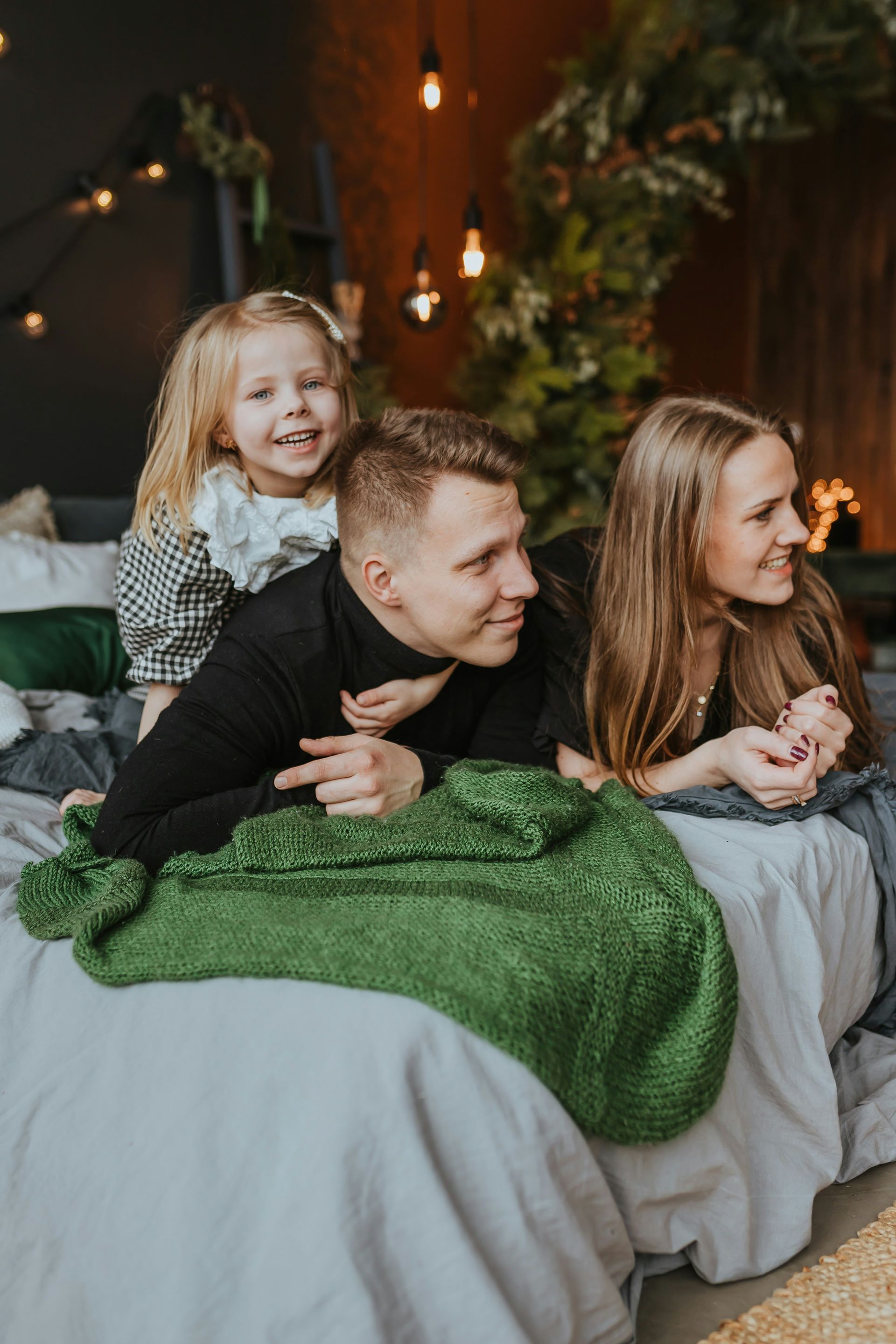 A family is sitting on a bed with a christmas tree in the background.