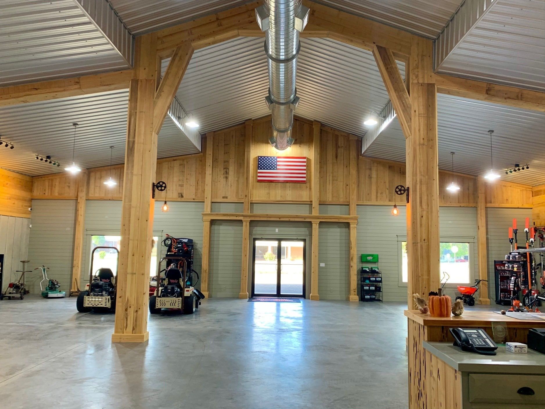 Open interior of a workshop or garage with wooden beams, concrete floor, and an American flag.