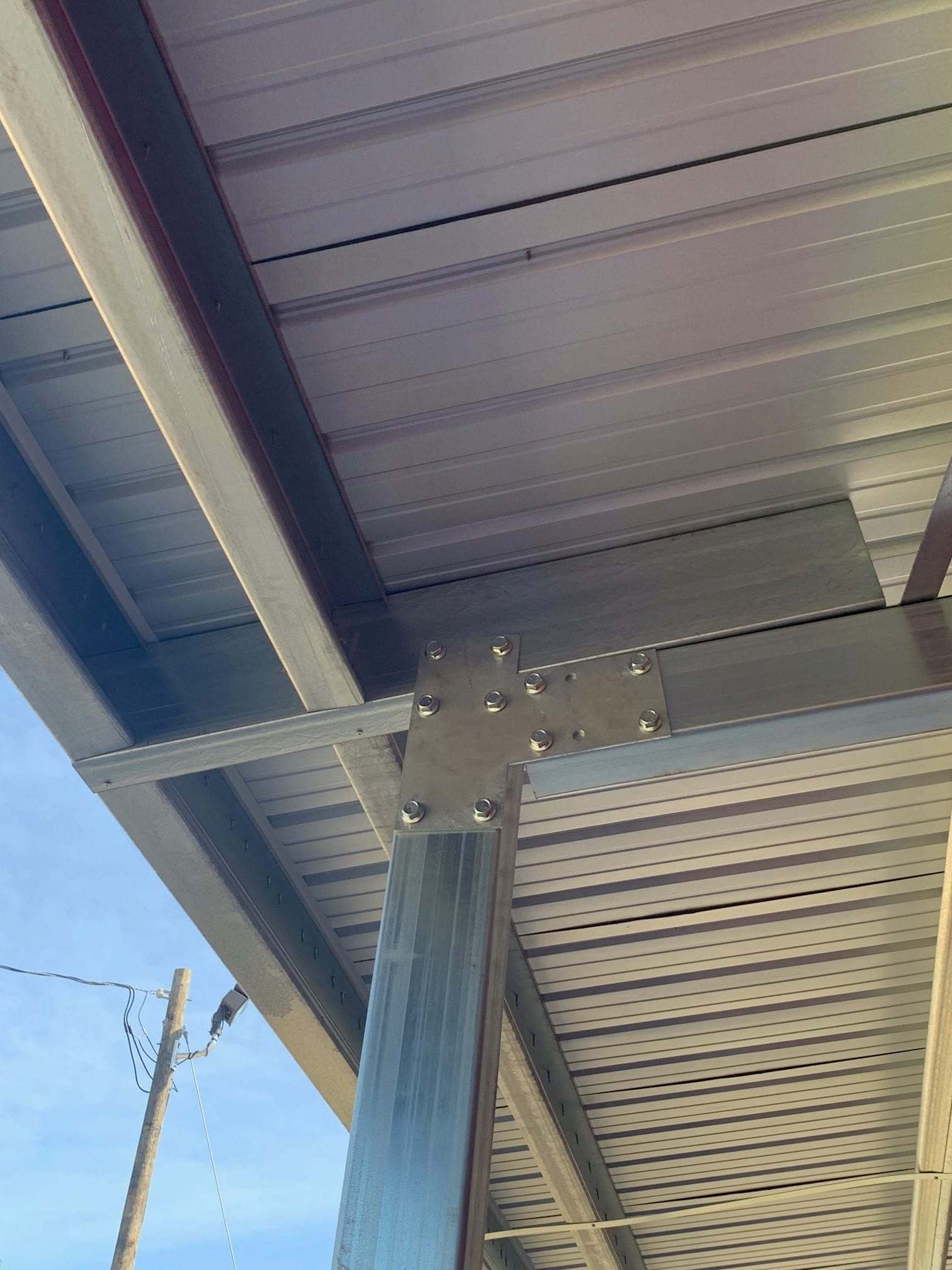 Metal framework supporting a corrugated metal roof. A structural bracket connects a vertical beam to horizontal supports.