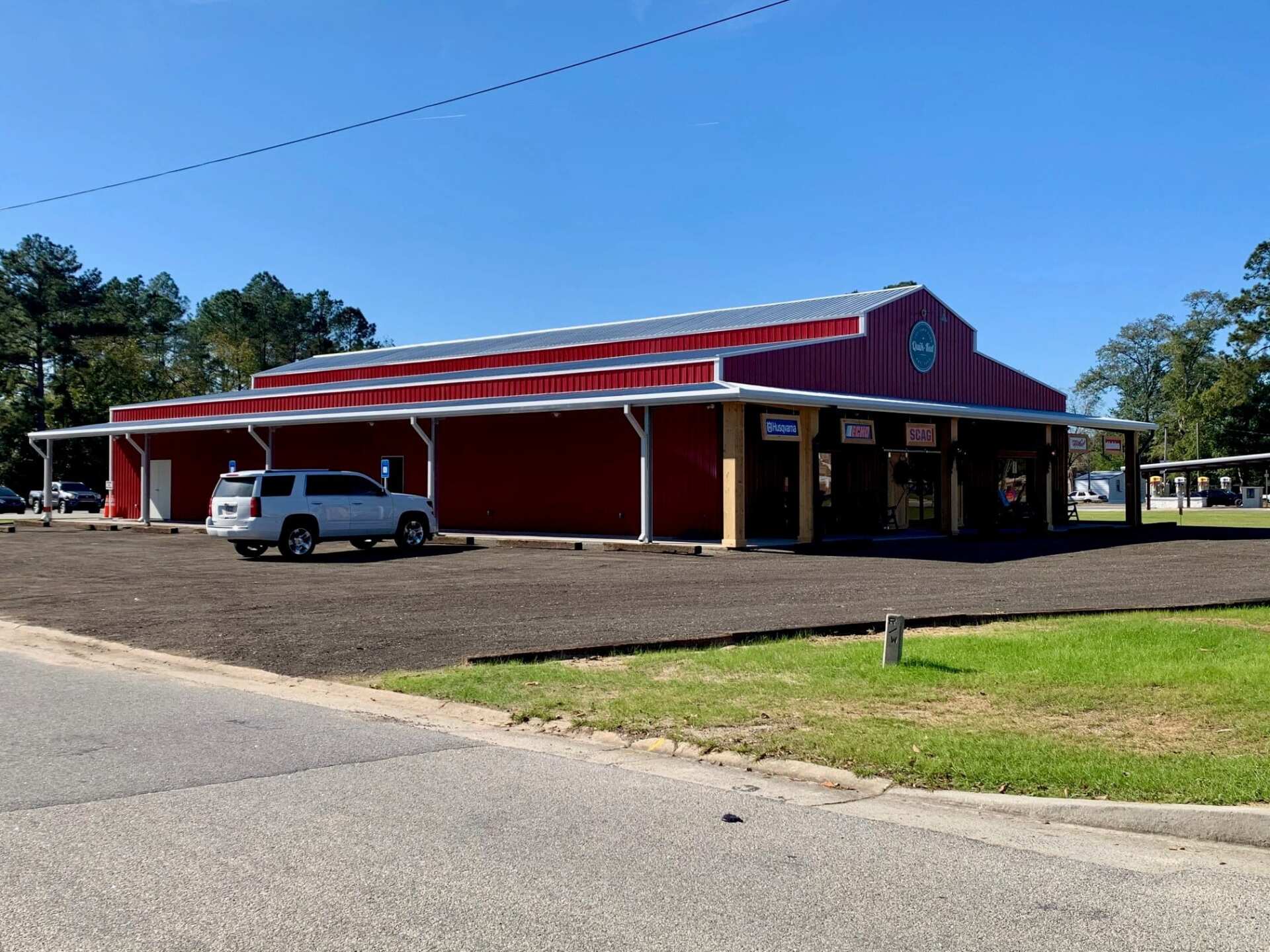 Red barn-shaped building with a white car parked in front on a sunny day.