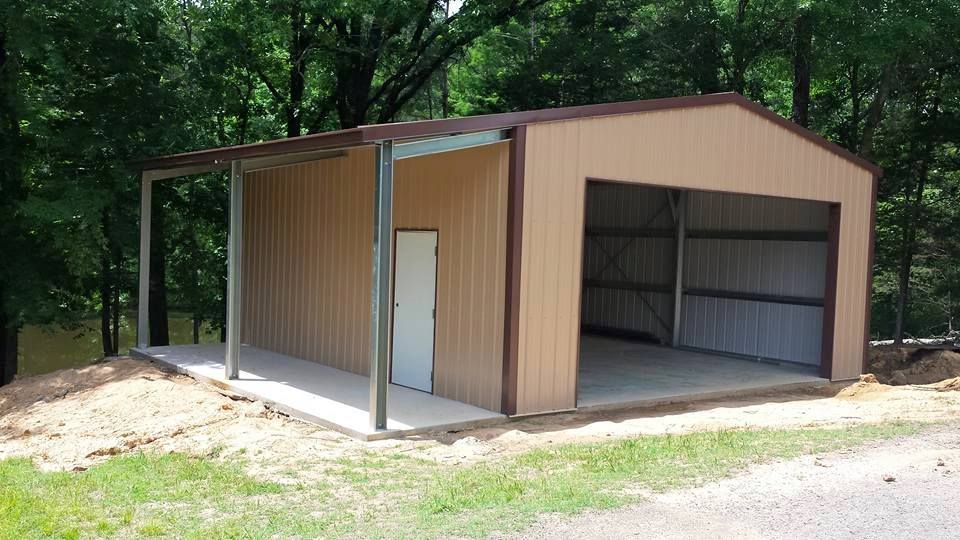 Tan metal garage with a covered porch, door, and open bay, set in a wooded area.