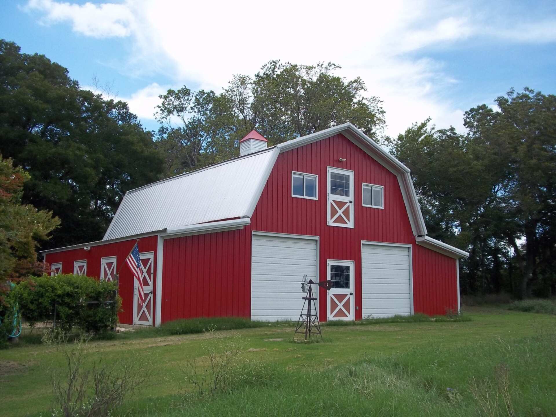 Red barn with white trim and roof, American flag, set in a grassy field.