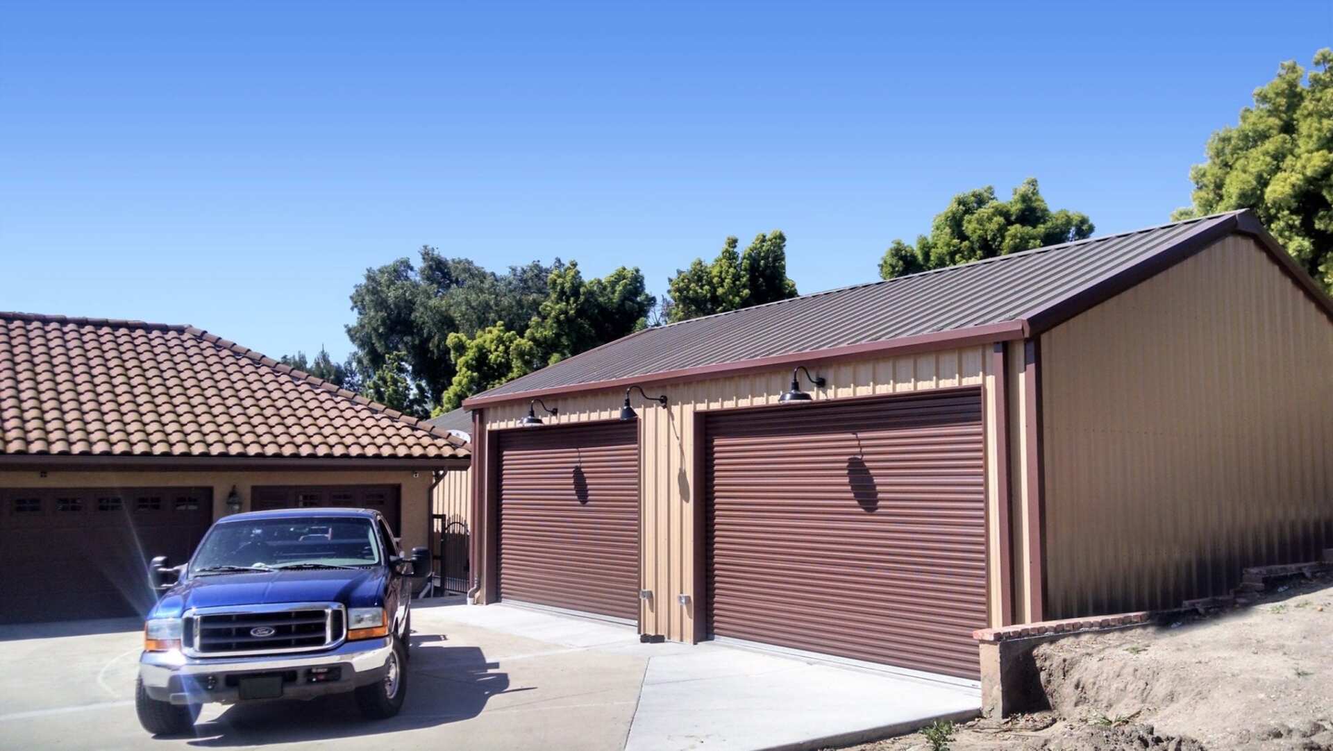 Blue truck parked in front of tan garage with two brown doors under a clear blue sky.