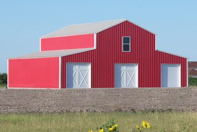 Red barn with white doors and a silver roof against a blue sky.