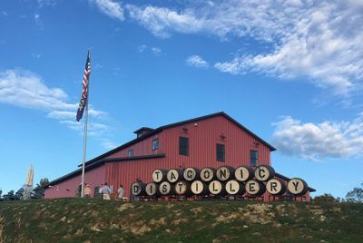 Taconic Distillery in a red barn, under a blue sky with a flagpole and barrels.