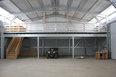 Metal building with a loft and wooden staircase. An ATV, a cat, and a workbench are visible below.