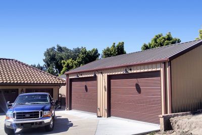 Blue truck parked in front of a two-car garage with brown doors and tan siding.