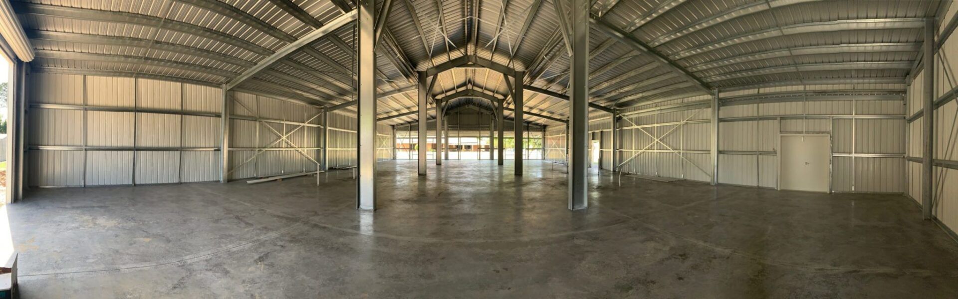 Empty industrial warehouse with arched metal roof and concrete floor.