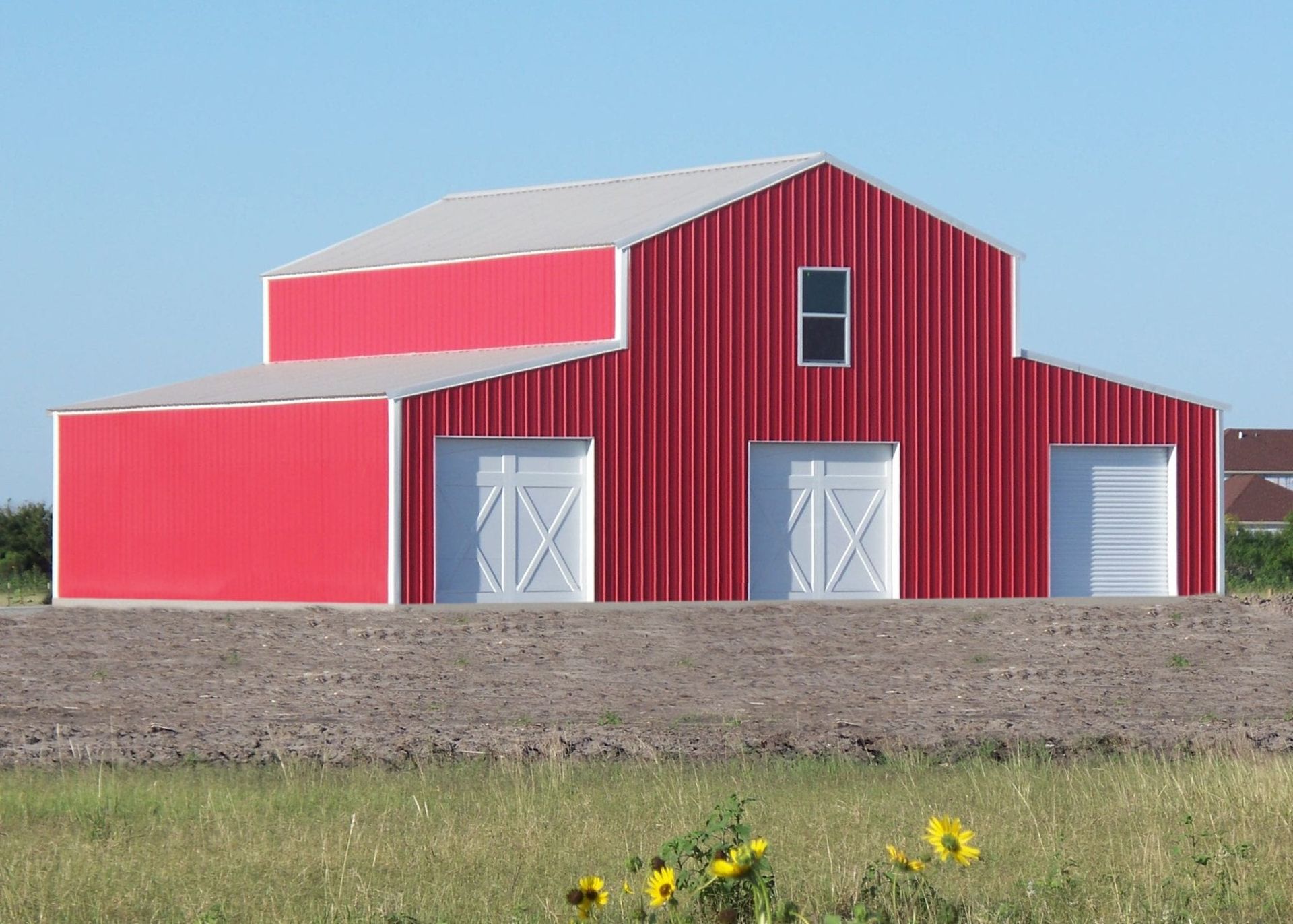 Red barn with white doors and roof against a blue sky; sunflowers in the foreground.