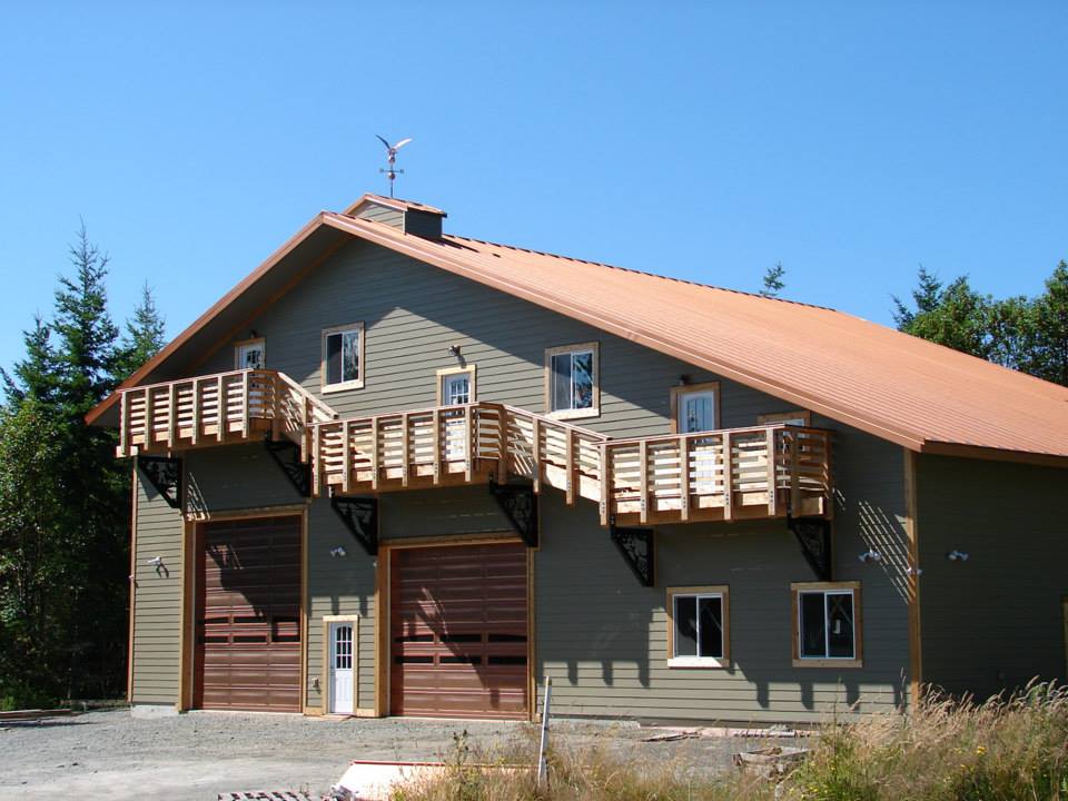 Two-story green building with brown roof and garage doors, connected by wooden balconies.