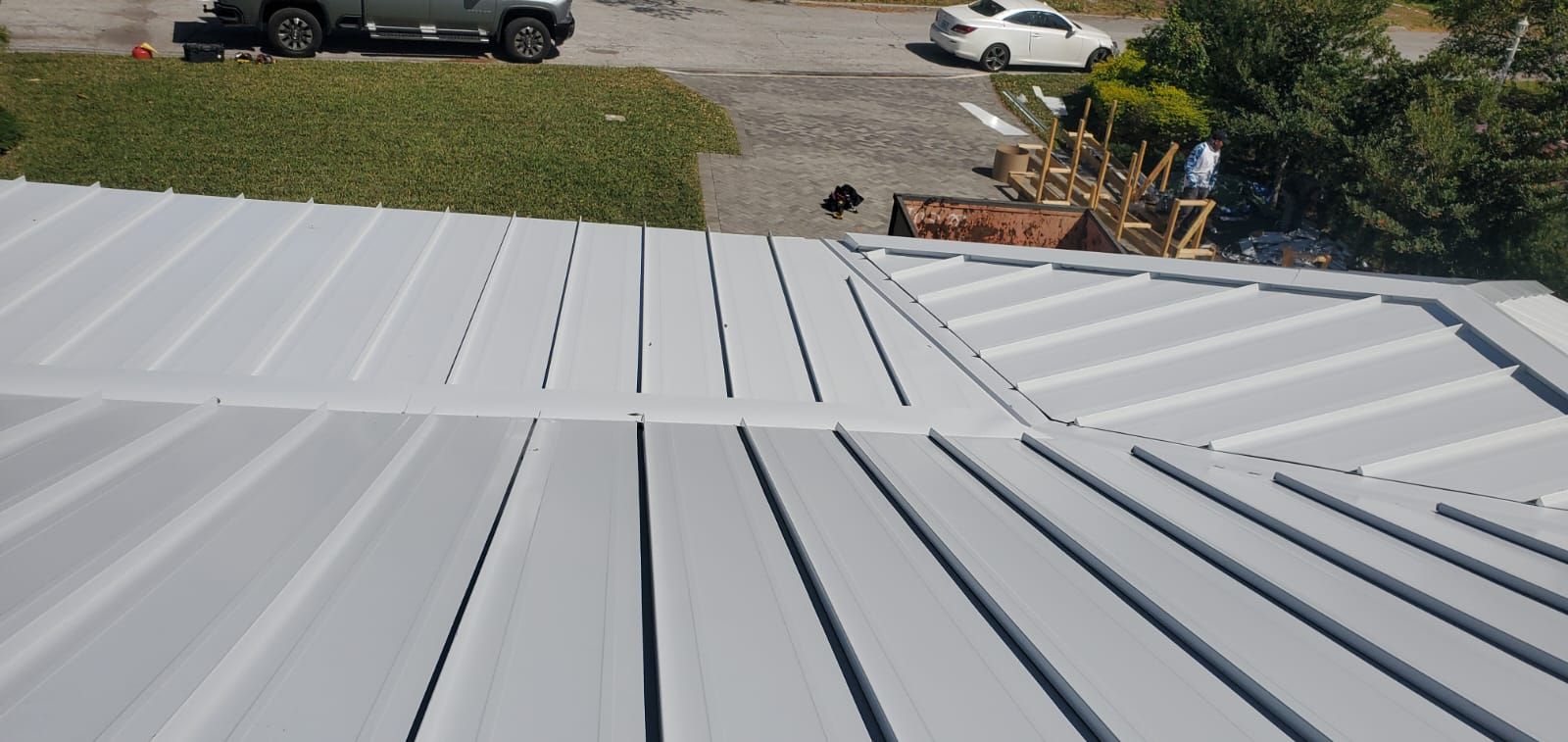 Gray metal roof with visible seams; green lawn and vehicles in the background.