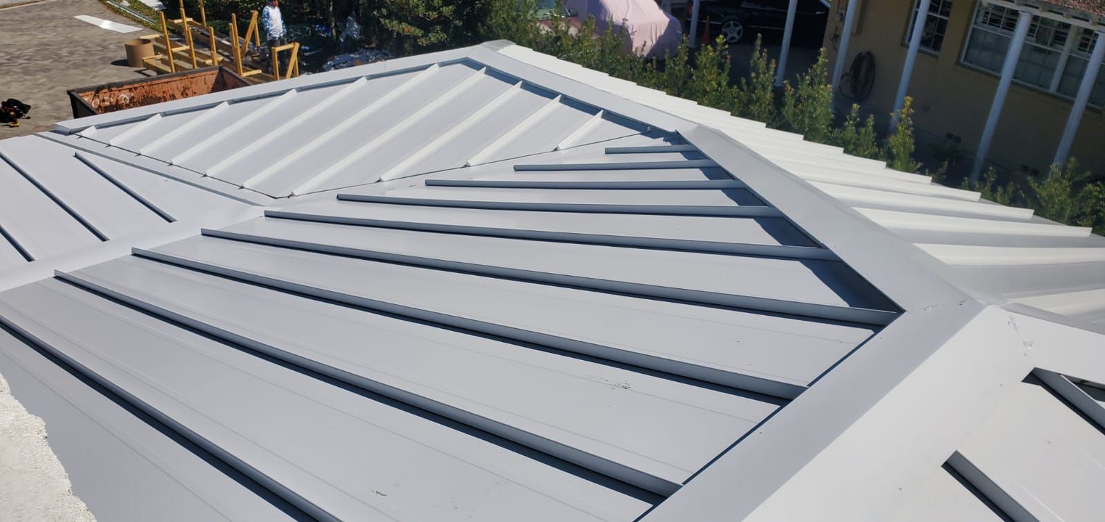 Metal roof with light gray panels and ridges. Angled view, sunny exterior.