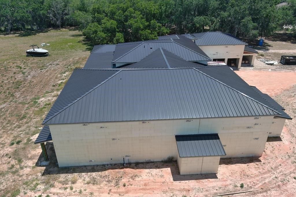 Exterior view of a large, modern house with a dark metal roof and a surrounding dirt yard.