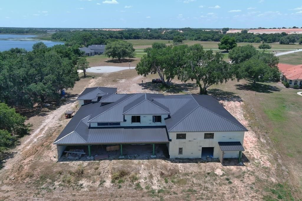 Aerial view of a house with a black roof, surrounded by trees and dry grass, near a lake.