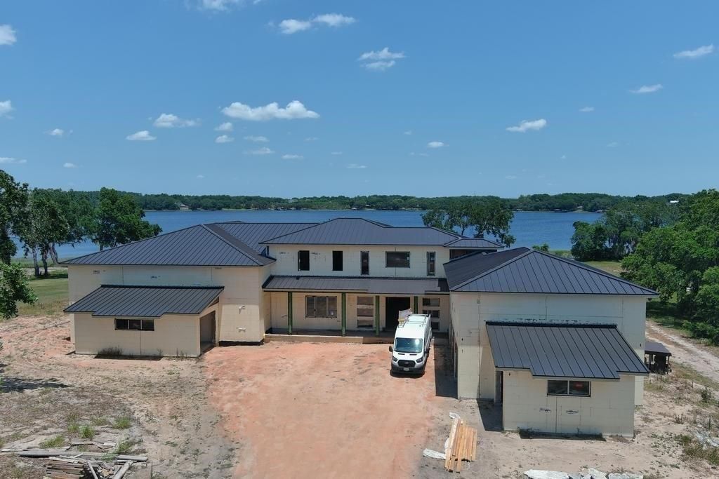 House under construction with a white van parked in front; a lake and blue sky in the background.
