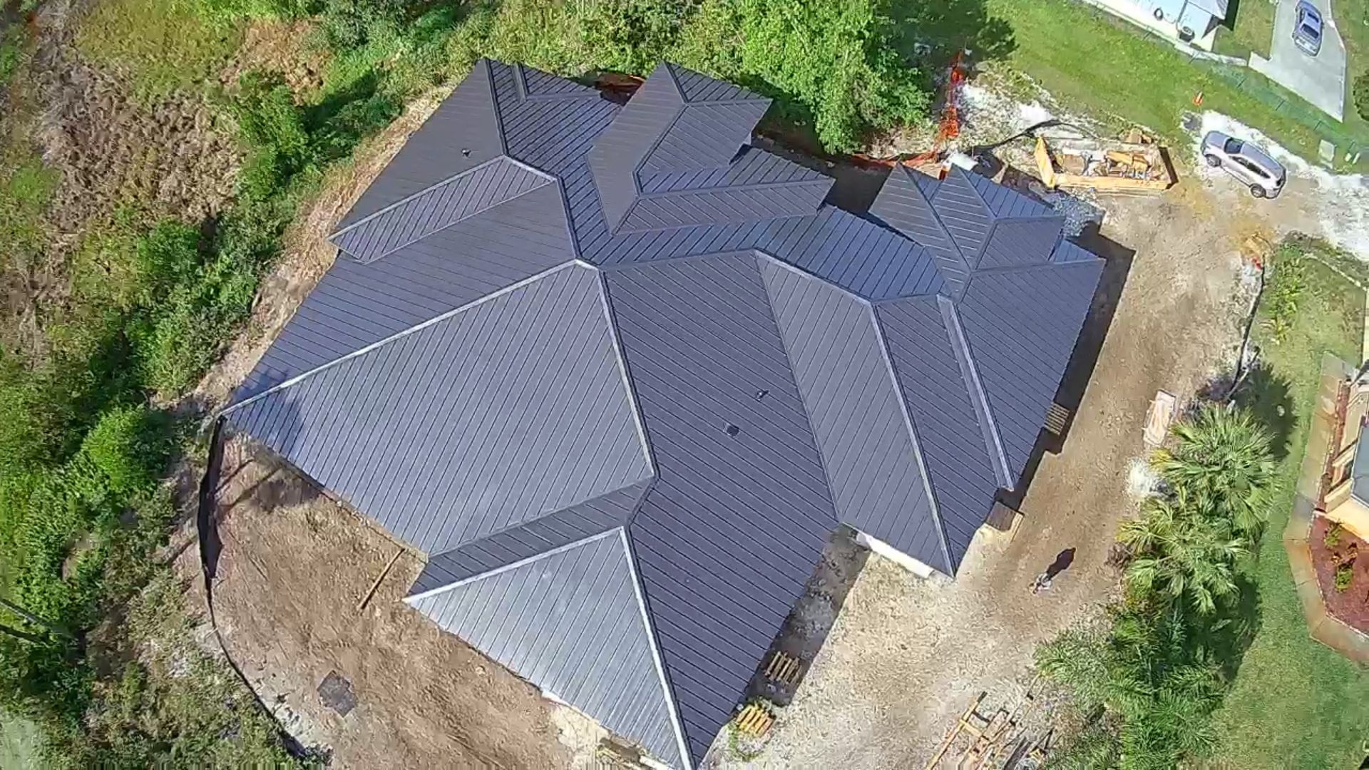 Aerial view of a dark gray roof of a house under construction, set in a grassy area.