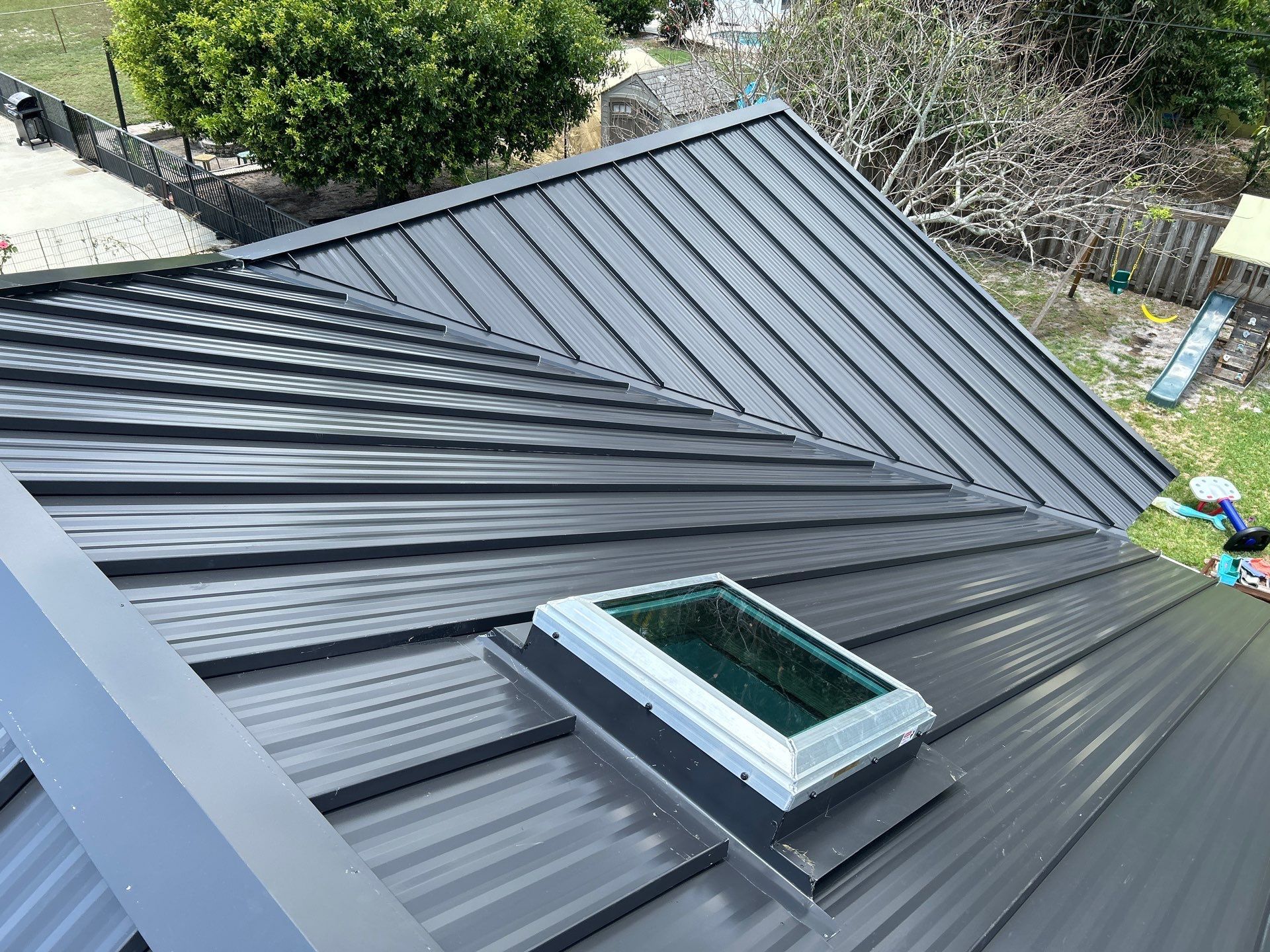 Dark gray metal roof with a skylight, viewed from an angle.