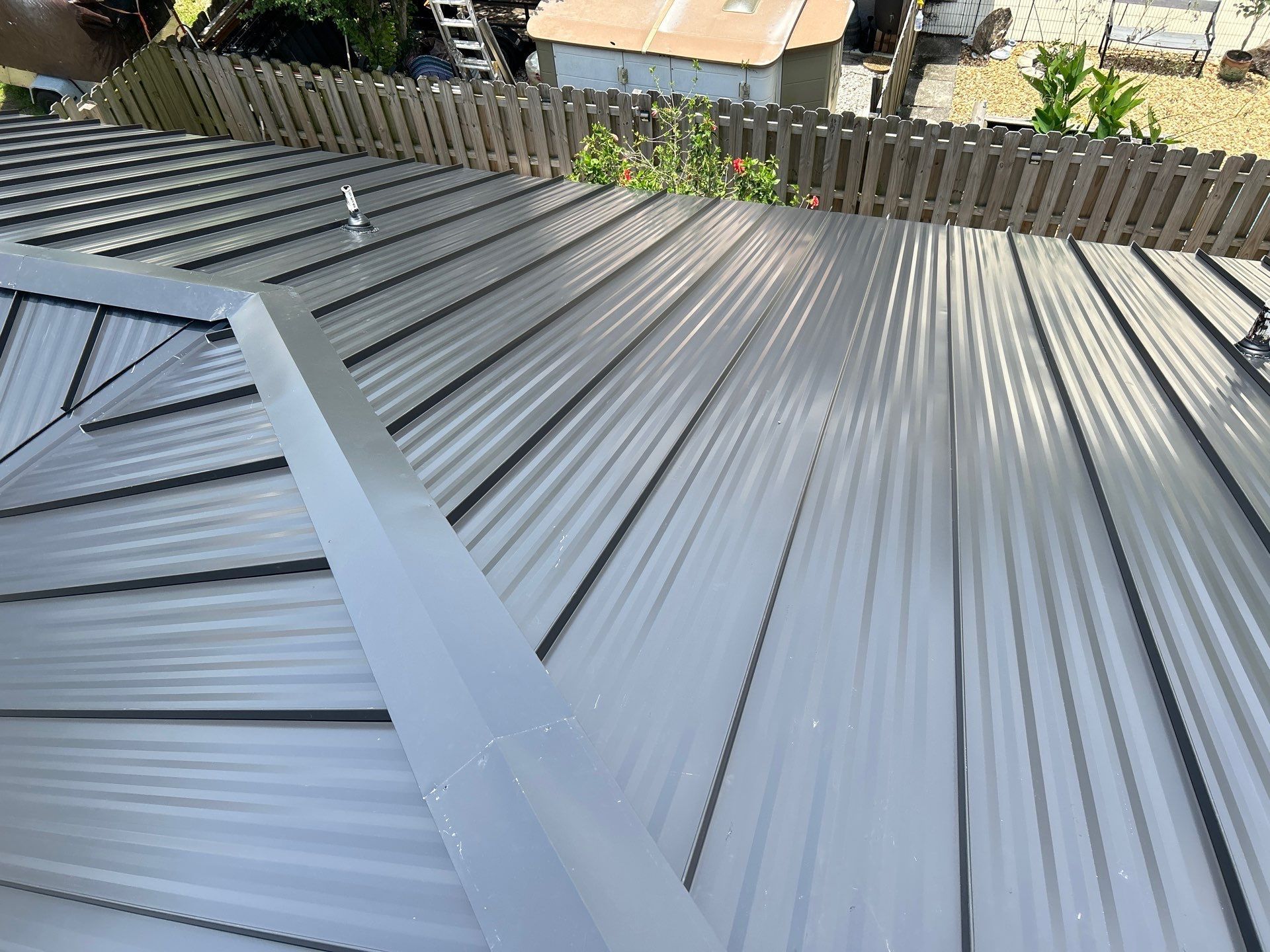 View of a gray metal corrugated roof with a fence and building visible in the background.
