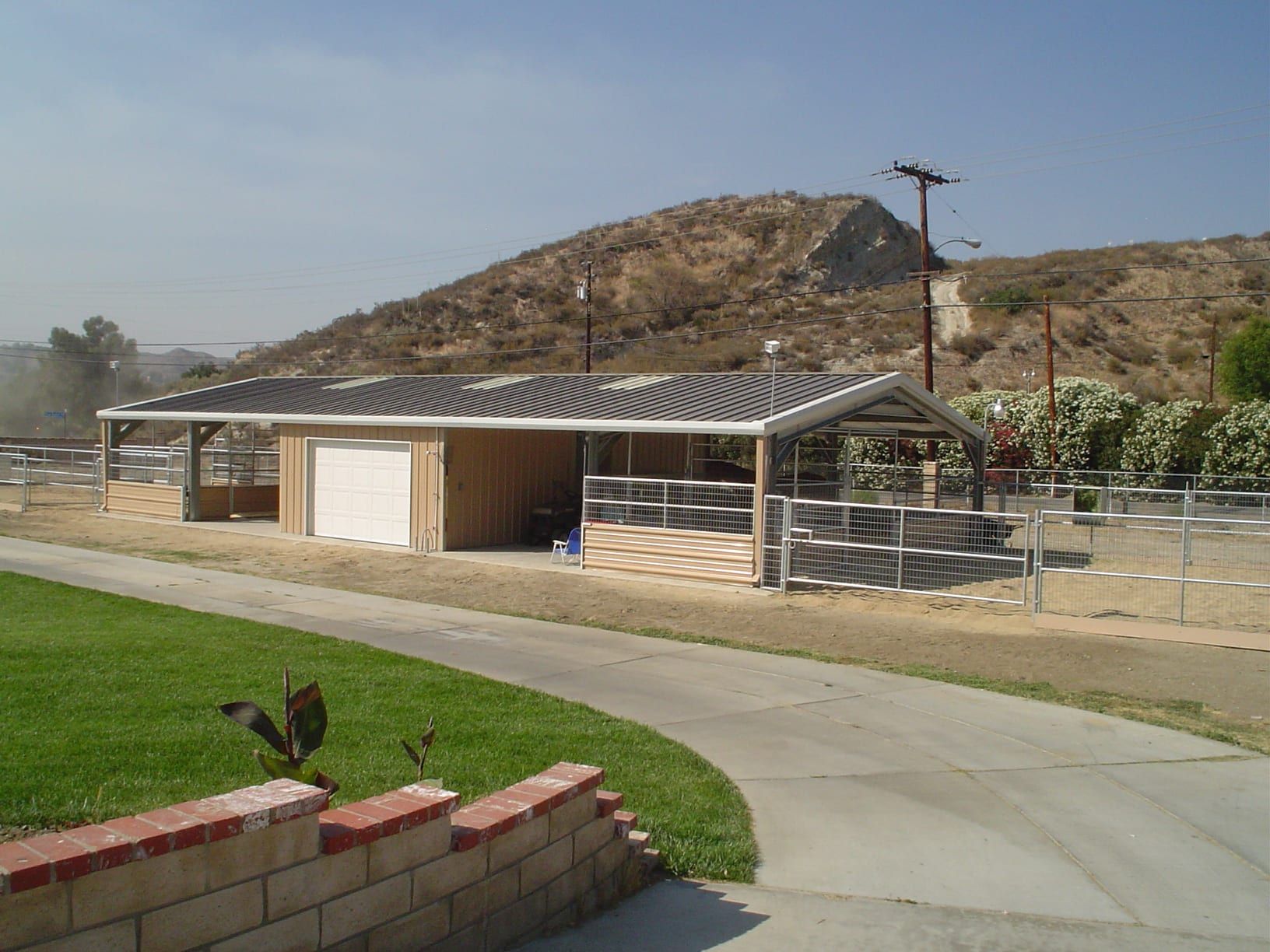 Horse stable with stalls, garage door, and roof, set against a hillside and clear sky.