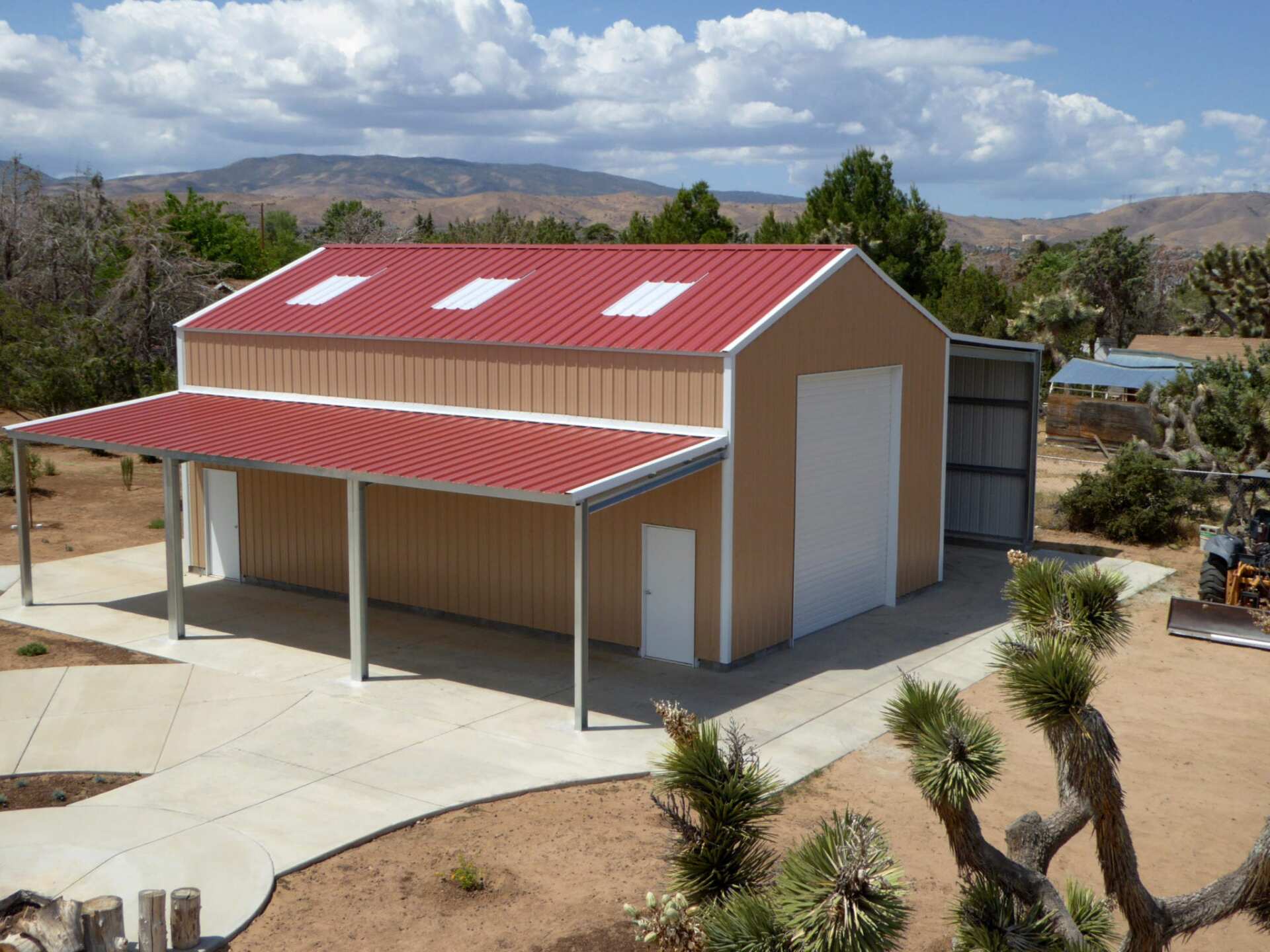 Tan metal barn with red roof, white doors, and carport. Desert landscape.