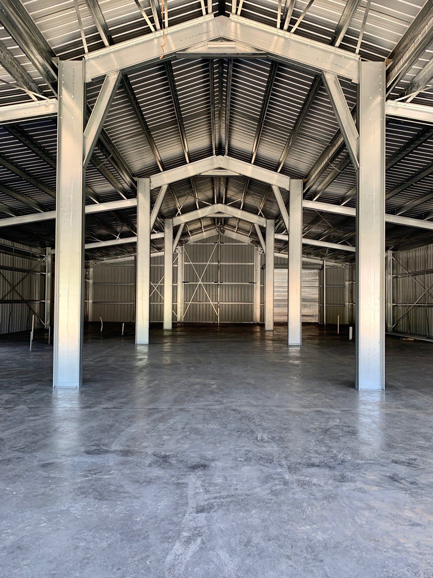 Empty metal warehouse interior, silver beams, concrete floor, arched ceiling.