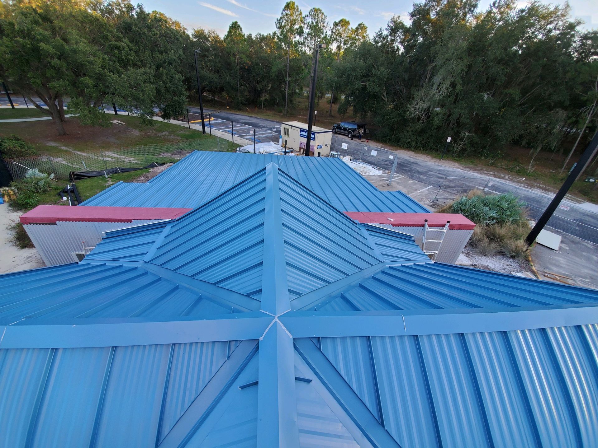 Blue metal roof with a cross pattern against a backdrop of trees and a road.