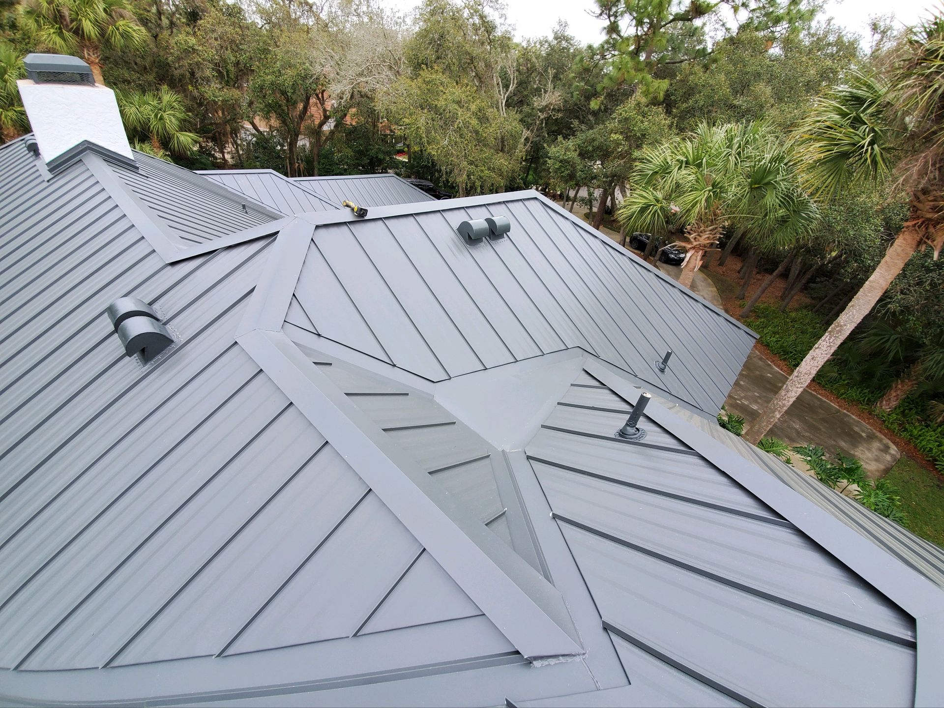 A metal roof, grey and ridged, on a house surrounded by trees.