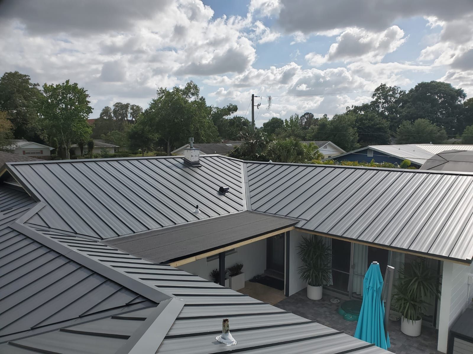 A modern house with a silver metal roof and an open courtyard. Cloudy sky in the background.