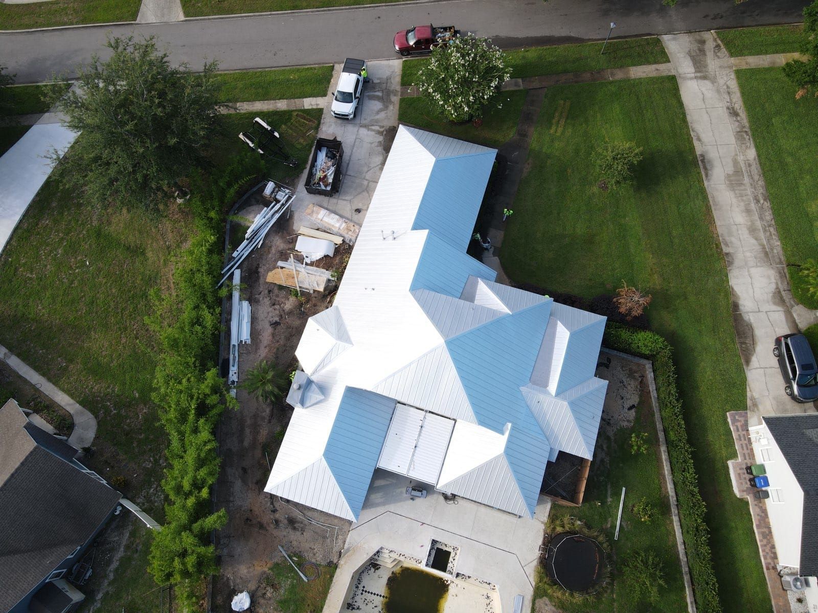 Aerial view of a house with a newly installed silver metal roof and construction materials in the driveway.