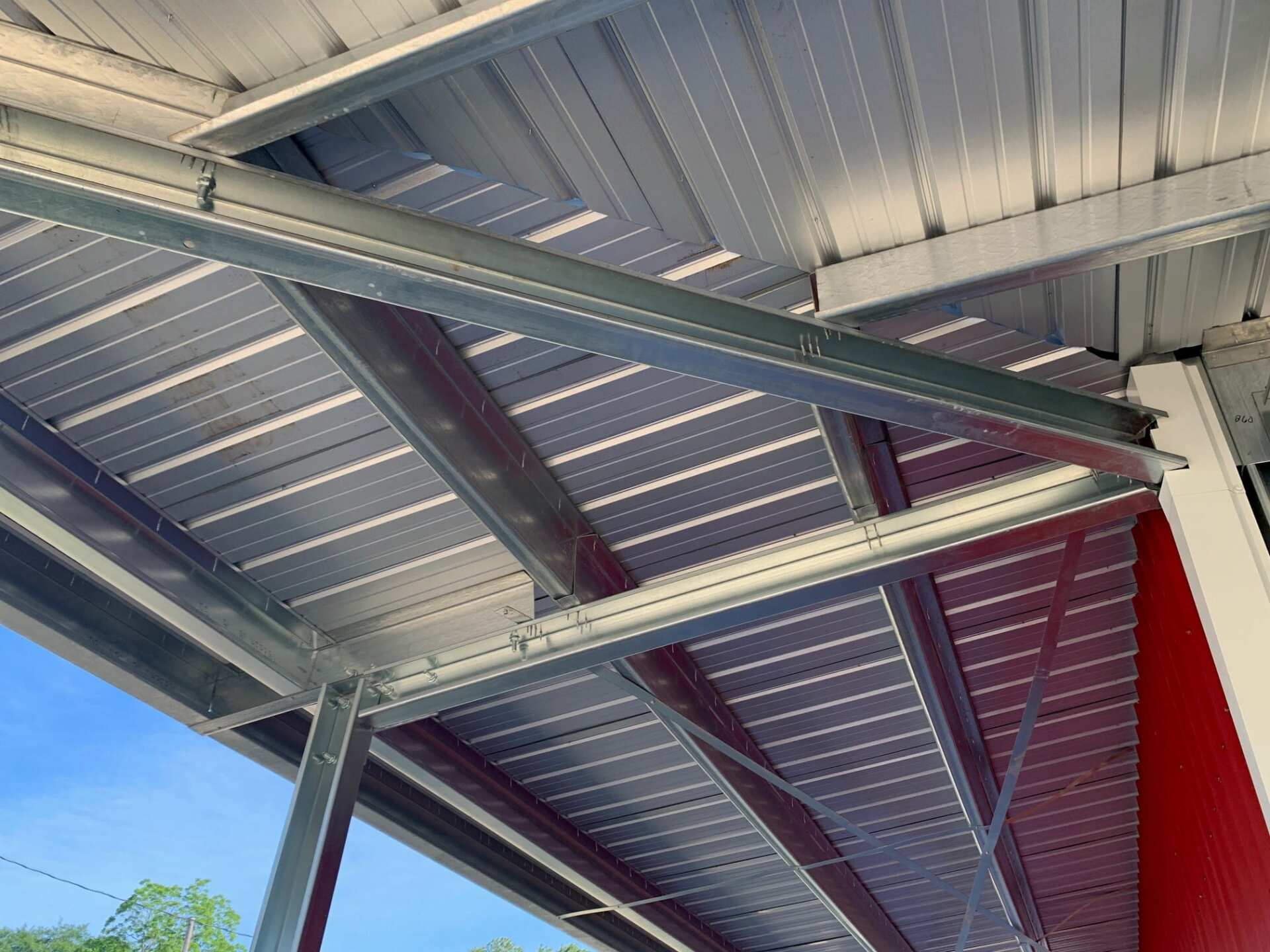 Metal roof structure with beams and panels, viewed from below, red and white walls.