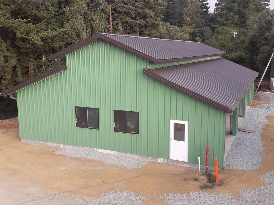 Green metal building with brown roof and trim; surrounded by gravel, with a door and windows.