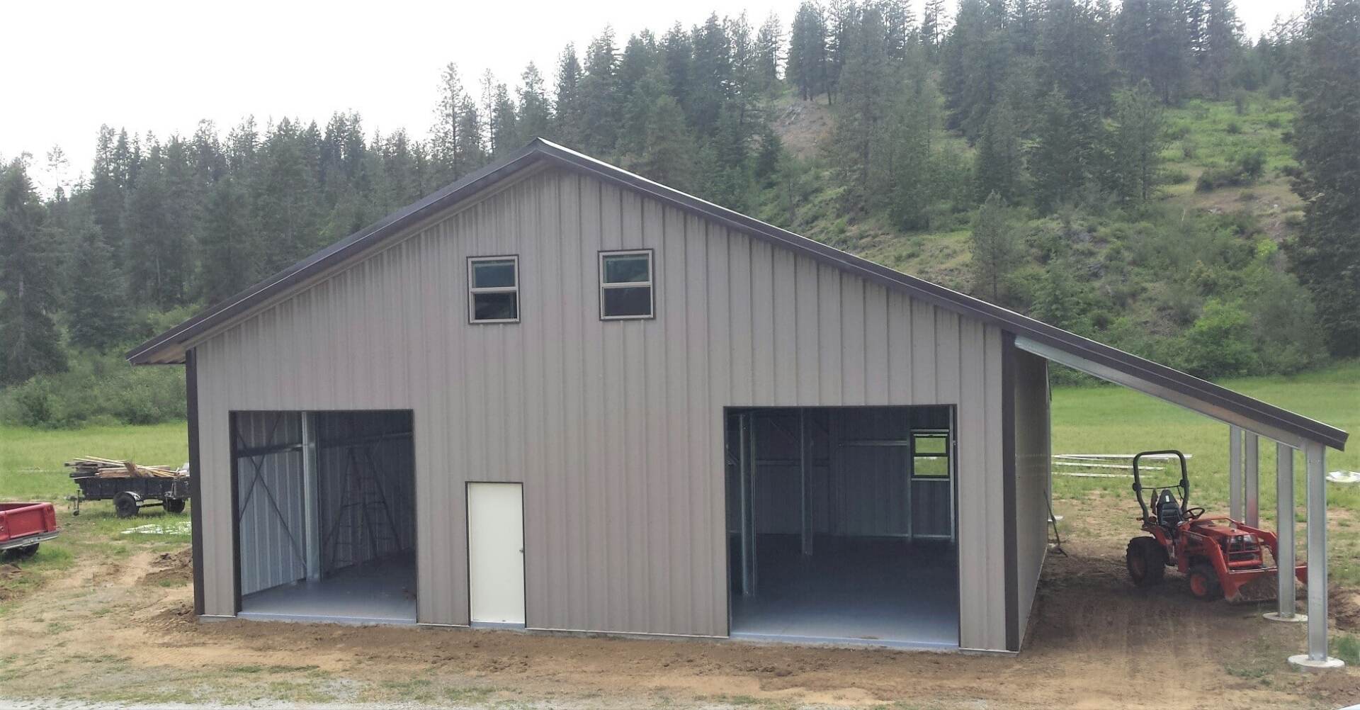 Gray metal barn with two bays, a lean-to, and windows, in a rural setting.