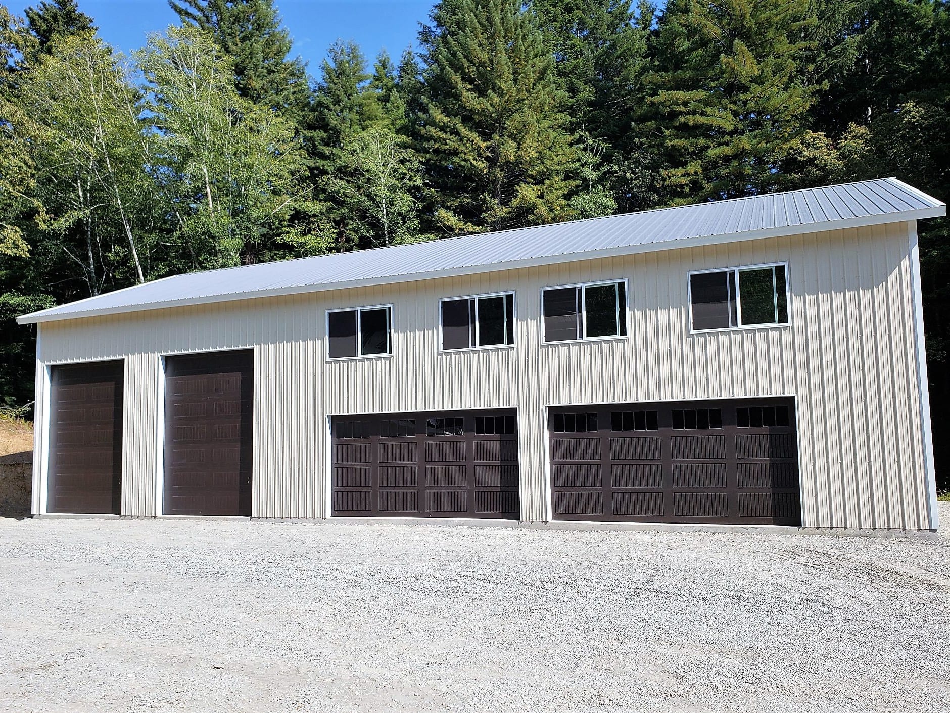 Light-colored, multi-bay garage with dark garage doors and windows, set against a backdrop of trees.