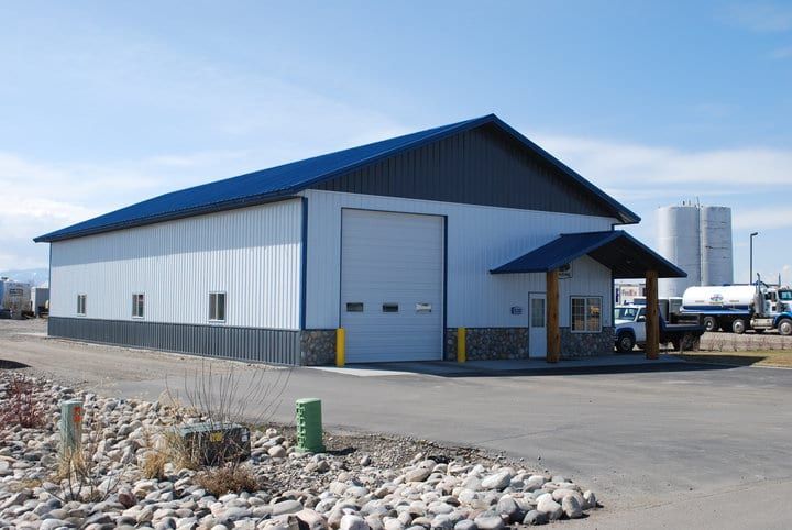 Metal building with blue roof, garage door, small entryway. Light blue/gray siding with dark gray base.