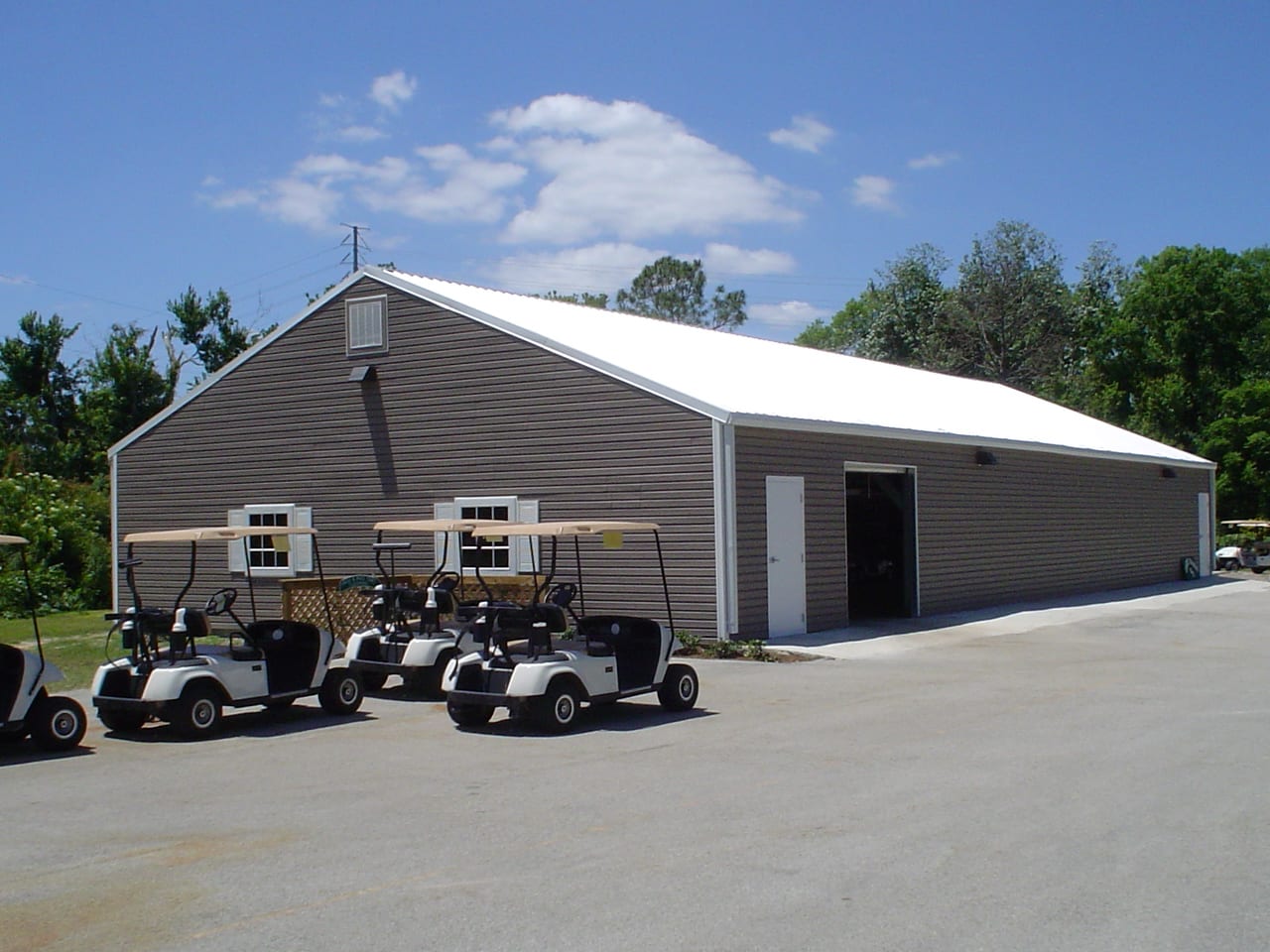 Golf carts parked in front of a brown building with a white roof. Sunny day.