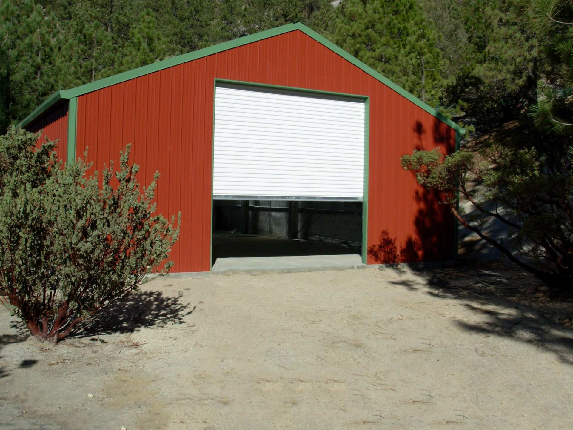 Red barn with open white garage door in a sandy area, green trees in the background.