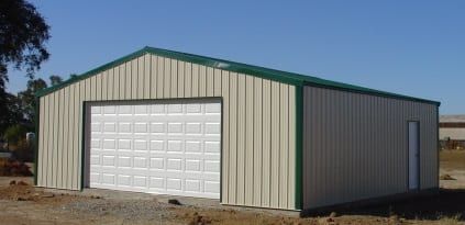 A beige metal building with a green roof and trim, a white garage door, and a small side door, outdoors.