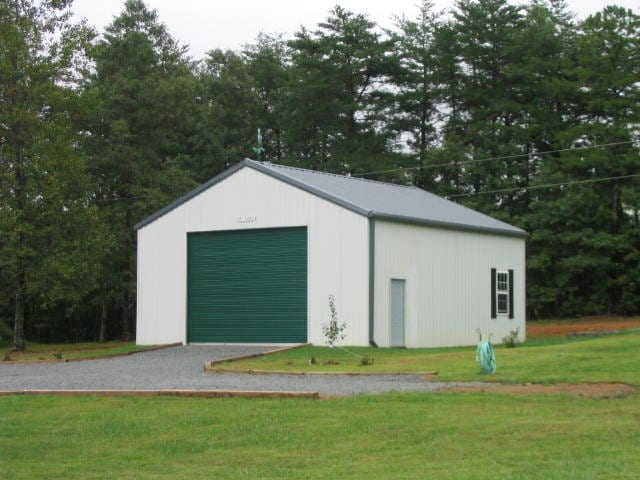 White metal garage with green door and gravel driveway on grassy property.