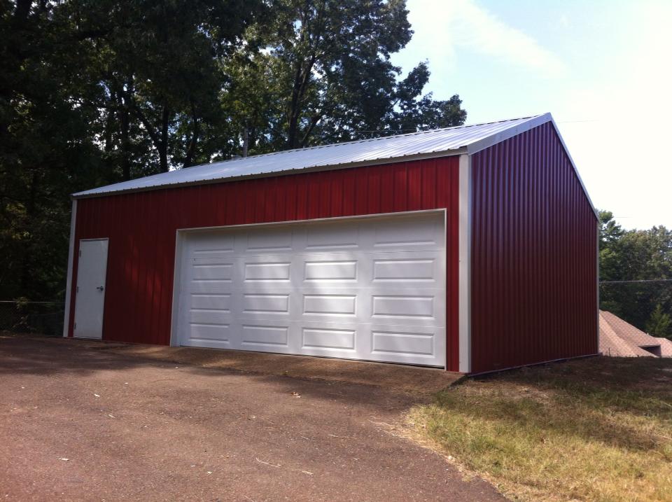 Red metal garage with a white garage door and white trim, set on asphalt driveway.