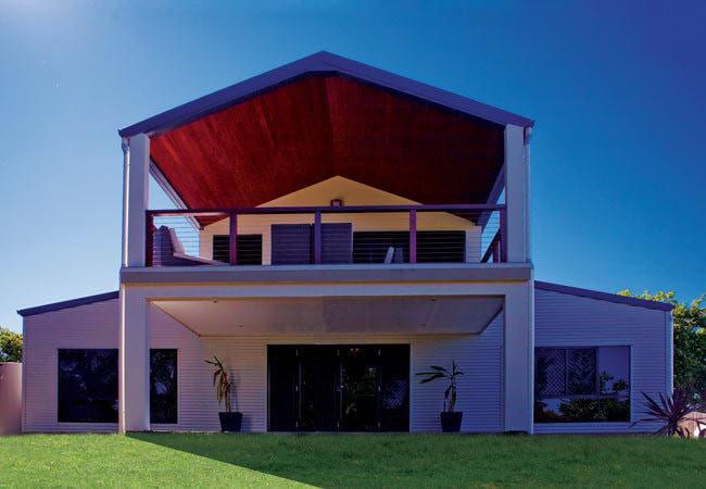 Two-story house with a red-lined porch, dark windows, and a green lawn under a blue sky.