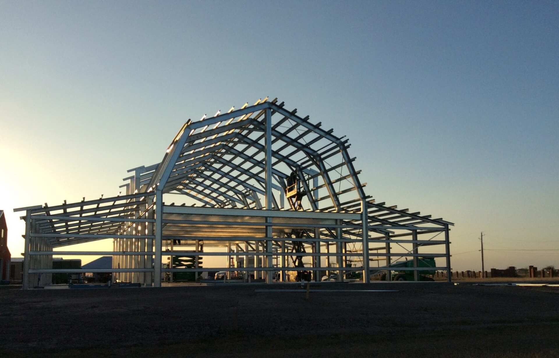 Steel frame of a large building under construction with arched roof in a sunny setting.