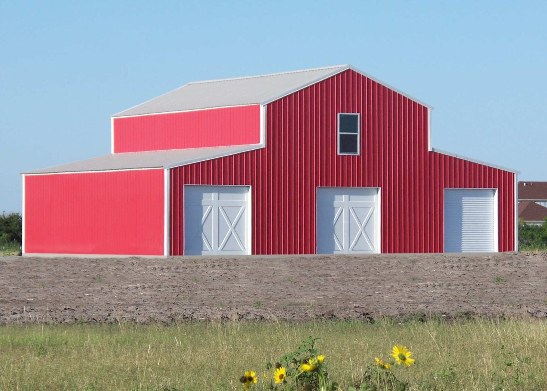 Red barn with white doors and a metal roof, set against a blue sky and field.