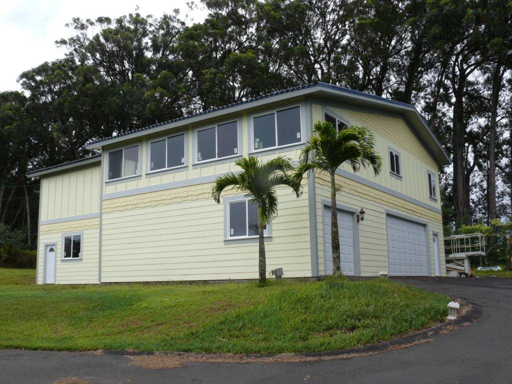Two-story light yellow building with multiple windows, a garage door, and palm trees on a grassy lawn.