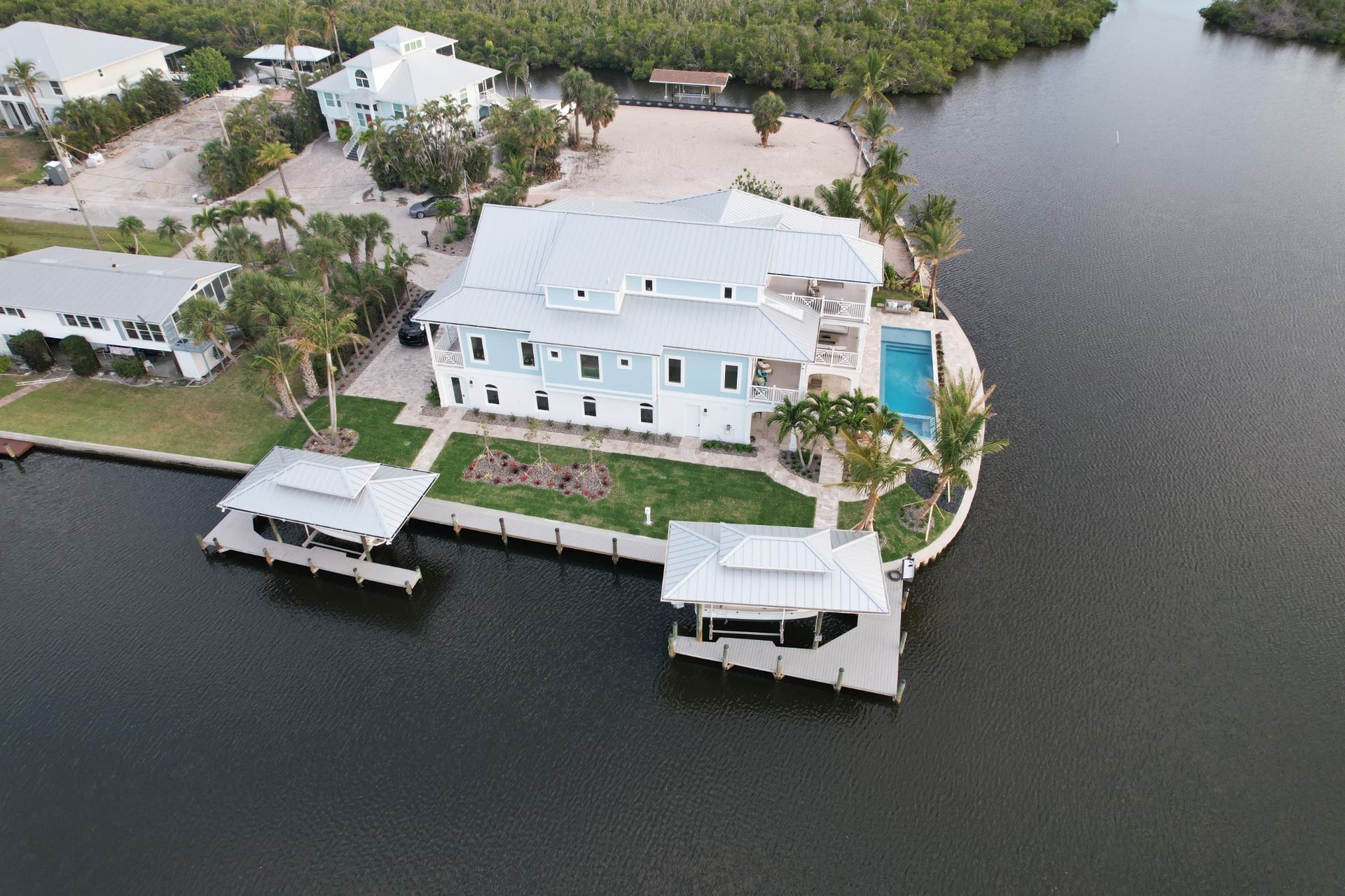 Large house on water with docks and pool. Blue siding, gray roof, green lawn, dark water.