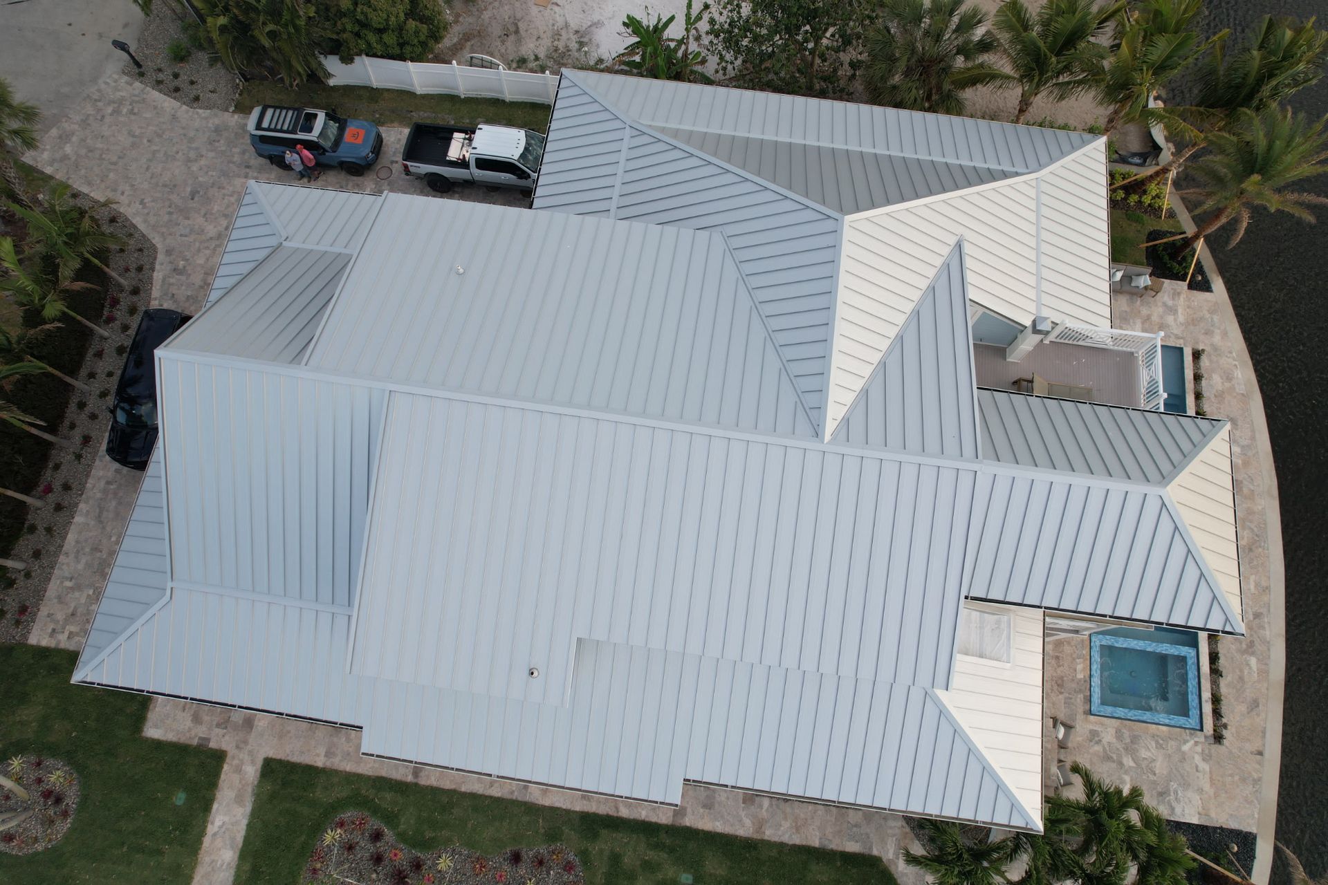 Aerial view of a modern house with a gray metal roof and surrounding greenery.