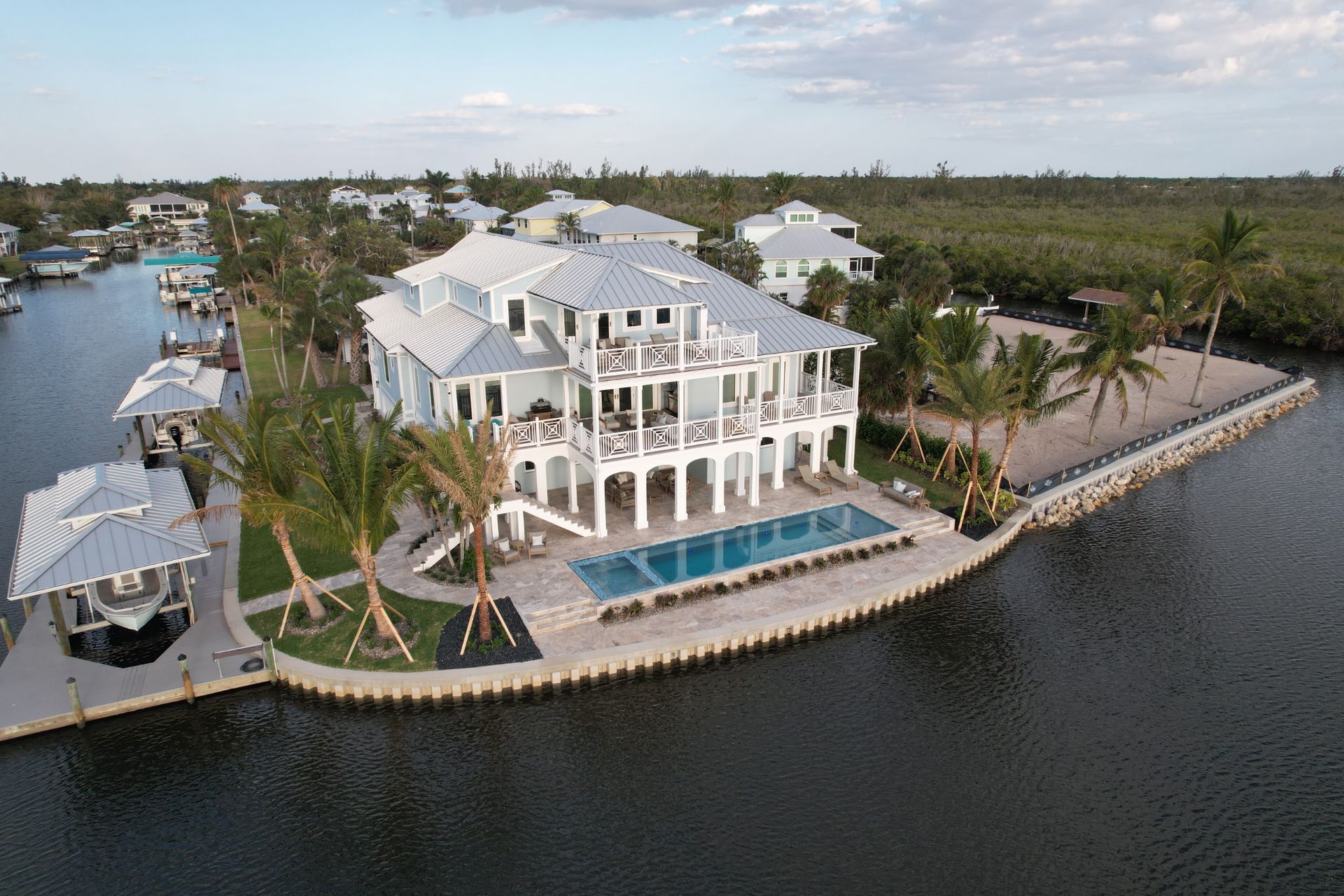 Aerial view of a large, multi-story light blue house with a pool, palm trees, and a dock on a canal.