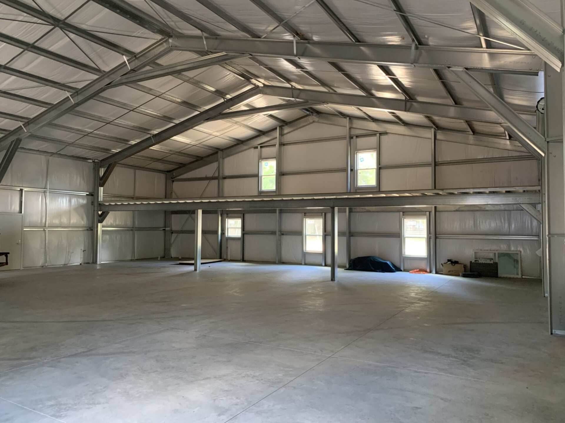 Interior view of a large, empty metal building with a concrete floor and windows, likely a warehouse.